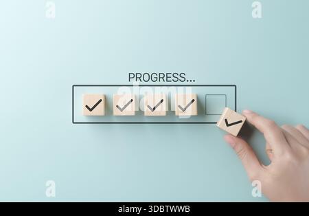 Checklist and task progress tracking concept. A hand placing the final checkmark on wooden blocks in a progress bar, task completion, productivity, go Stock Photo