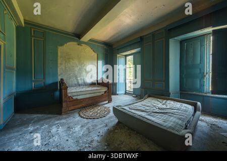 Sunlit abandoned château bedroom with antique beds, blue paneled walls and faded mural Stock Photo