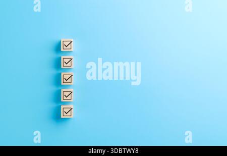 Checklist concept. Correct sign tick checkmark on wooden block with copy space for the checklist on light blue background. Business survey questionnai Stock Photo