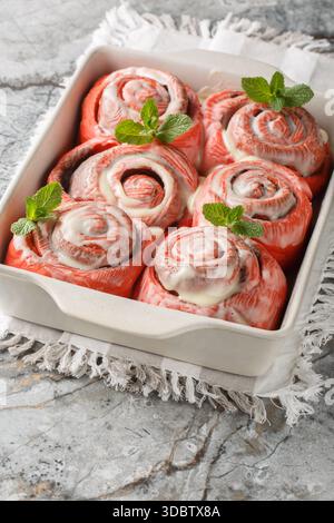 Close-up of pink cinnamon rolls with white icing in a baking dish on a table. Vertical Stock Photo