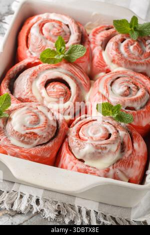 Freshly baked pink cinnabon buns with cream sauce  closeup on the baking dish on the table. Vertical Stock Photo