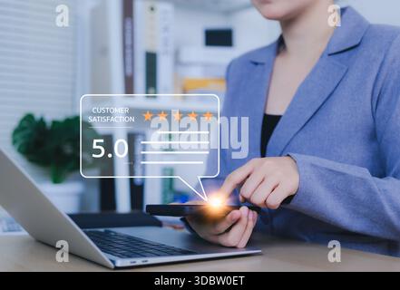 Customer review satisfaction feedback survey concept. A woman interacts with a smartphone, giving a five-star rating using a digital feedback system, Stock Photo