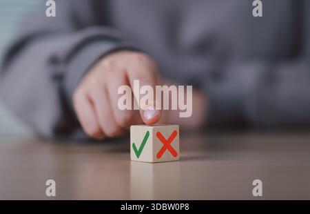Decision Making and Evaluation Concept. Hand points at wooden cube with green check and red cross symbols, represent decision-making true and false, r Stock Photo