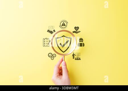 Work Safety and Compliance Concept. Magnifying glass over shield with check mark surrounded by icons symbolizing workplace safety, inspection, Stock Photo