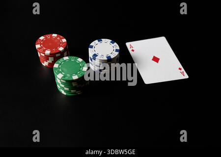 Studio shot of an ace of diamonds playing card next to stacks of red, green, and blue poker chips on a black background. Casino gambling concept with Stock Photo
