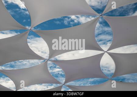 An abstract pattern created by sun shade sails against a cloudy blue sky in Tavira, Portugal Stock Photo