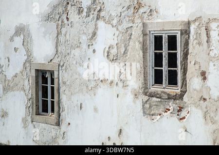 Two windows in an old and damaged rendered wall of a building in the town of Tavira, Algarve, Portugal Stock Photo