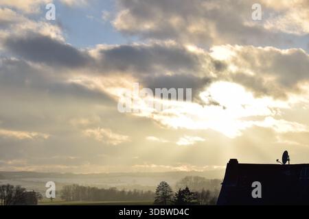 sinking sun in gray clouds above winter landscape Stock Photo