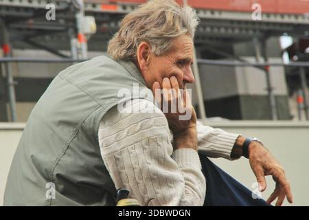September 2015 side profile shot of an older man with grey hair, wearing a white knitted sweater and a light green vest, sitting and resting his chin Stock Photo