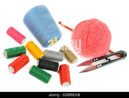 A vibrant collection of colorful sewing thread spools, a soft pink yarn ball, and tailoring scissors on a white background. Stock Photo