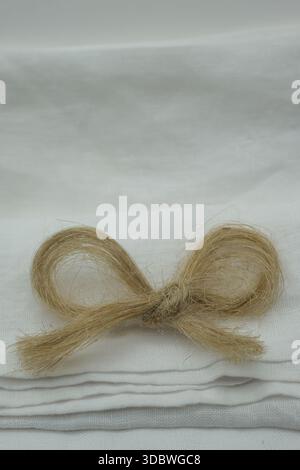 Flax fiber filament in the shape of a bow on folded snow-white linen fabric. Flax bleaching technology. Minimalism. Copy space. Stock Photo