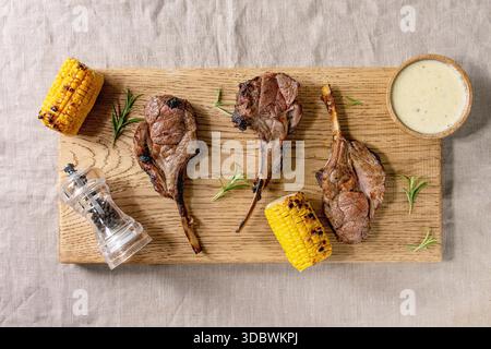 Grilled bbq rack of lamb with sweet corn cobs, rosemary and cheese sauce on wooden cutting board on linen cloth background. Flat lay, space Stock Photo