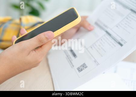 woman use phone scan barcode or QR codes to pay credit card bill after receiving document invoice. payment, receive, paying electricity, digital payme Stock Photo