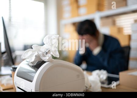 Label printer malfunction on work desk while stressed warehouse owner faces business problems and operational failure in storage office || Model released Stock Photo