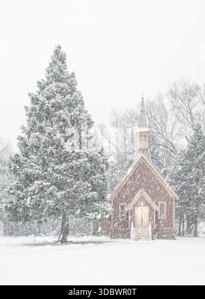 View of a quaint red chapel stands nestled amidst snow-laden trees, its warm light a beacon in the serene, wintry landscape, Yosemite Valley, Californ Stock Photo