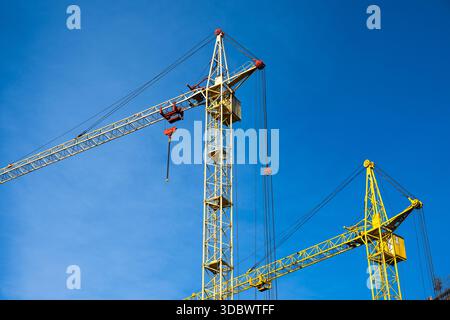 Two yellow construction cranes against  blue sky . Stock Photo