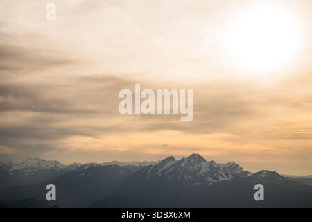 View of snow-capped mountain peaks pierce through a blanket of clouds under the warm glow of the sun, Rigi Kulm, Lucerne, Canton Lucerne, Switzerland. Stock Photo