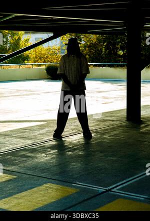 A man wearing a hat and a patterned shirt stands with his hands clasped in front of him. Stock Photo