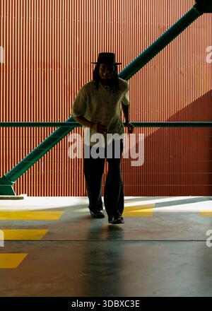 A man wearing a hat and casual clothing is walking towards the camera. Stock Photo