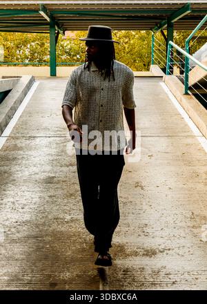 A man wearing a hat and casual clothing walks towards the camera on a concrete ramp. Stock Photo