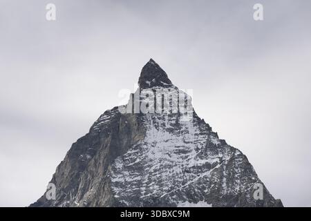View of the imposing Matterhorn peak, a jagged silhouette against a soft, overcast sky, its snow-dusted slopes hinting at the alpine chill, Zermatt, V Stock Photo
