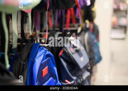 Colorful backpacks hang on display in a retail store for customers to browse and shop for school supplies. Stock Photo