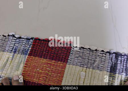 A person works on a colorful woven fabric laid out on a table. The focus is on the weaving process. Stock Photo