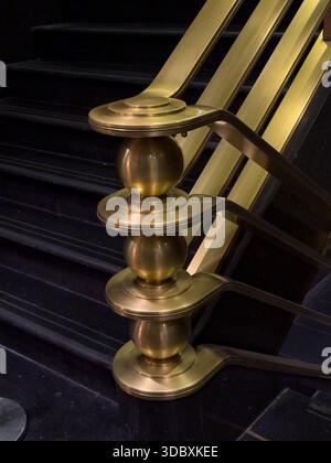 View of the gleaming golden handrail ascends beside the dark, sleek stairs, a contrast of warm metallic tones against the cool, deep shadows, New York Stock Photo