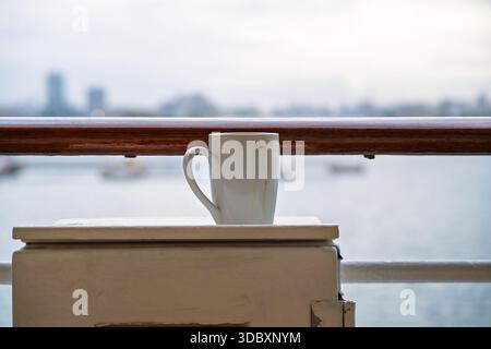 Morning coffee gone rogue  left dirty and lonely on the ship's metal box by the railing. Stock Photo