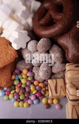 assorted sweets display with chocolates, marzipan cookies, dragees, and marshmallows in a colorful and tempting arrangement on soft purple surface, de Stock Photo