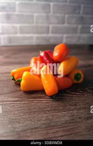 vibrant assortment of mini bell peppers stacked on rustic wooden surface with subtle brick background creating a warm and inviting still life composit Stock Photo