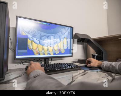 Dental technician using CAD software to design digital 3D model of patient teeth for prosthetic restoration. Stock Photo