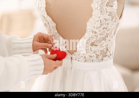 Female hands with pin cushion sewing wedding dress on mannequin in atelier, closeup Stock Photo