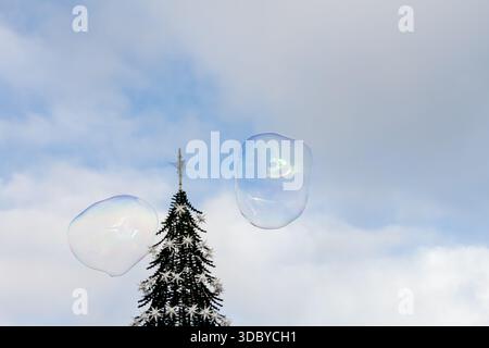 Two large soap bubbles drift in the sky above a decorated Christmas tree in Lisbon captured on a clear winter day Stock Photo