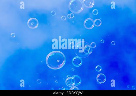 Small soap bubbles float upward against a bright blue sky with soft cloud patterns on a clear winter day. Stock Photo