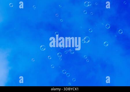 Dozens of soap bubbles drift across a deep blue winter sky with faint cloud patterns visible in the background. Stock Photo