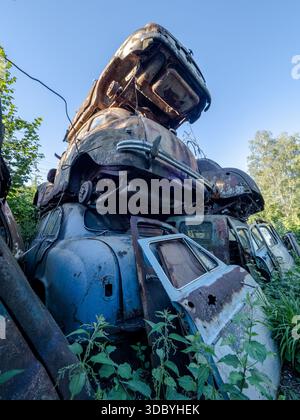 Stacked vintage vehicles in an overgrown Austrian car graveyard - rusted patina, peeling paint and corroded metal under a clear blue sky Stock Photo