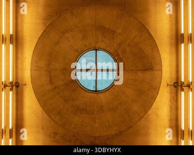 Circular skylight in concrete ceiling with blue glass and warm fluorescent lighting Stock Photo