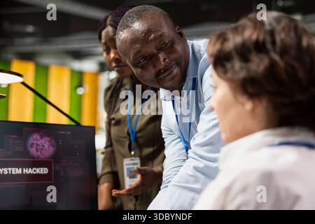 Startup office system administrator doing software debugging, helped by coworkers to fix virus. Female engineer fighting hacker ddos attack, being assisted by team members sharing advice Stock Photo