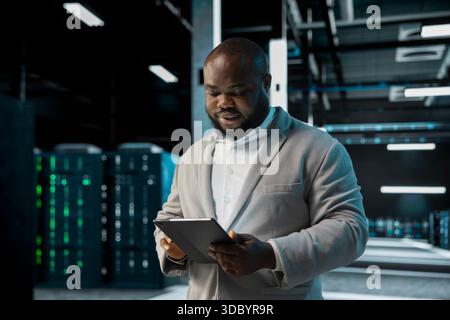 Server room IT professional doing infrastructure scans, fixing network issues affecting rigs performance. Data center programmer runs system diagnostic tests on tablet, tracking resource utilization Stock Photo