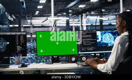 Female programmer talking with manager in data center, reviews AI diagnostics on green screen PC. IT expert and supervisor optimizes artificial intelligence systems using mockup computer, camera A Stock Photo