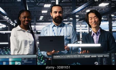 Portrait of smiling engineers in data center code with generative AI assistance. Happy IT experts doing brainstorming, leveraging artificial intelligence large language model to solve tasks, camera A Stock Photo
