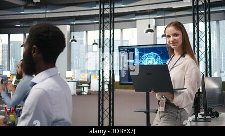 Portrait of young smiling female programmer in office automating repetitive tasks using AI scripts. Cheerful junior developer using artificial intelligence to speed up feature implementation, camera A Stock Photo