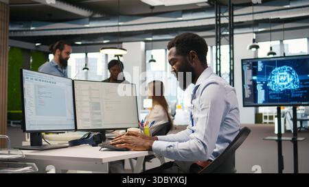 System administrator in tech startup office using PC, troubleshooting hardware and software issues. IT professional at work monitoring and optimizing performance using computer, camera A Stock Photo