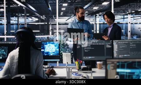 Data center manager supervising work done by programmers working on neural network software. Server hub supervisor overseeing IT staff members implementing deep learning tech, camera A Stock Photo