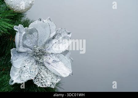 A silver flower decoration is placed on a green Christmas tree branch. The scene shows a simple holiday setup indoors. Stock Photo