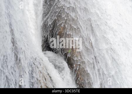 Detailed Close Up Of White Water Cascading Over Textured Brown Rock Face In Natural Light Stock Photo