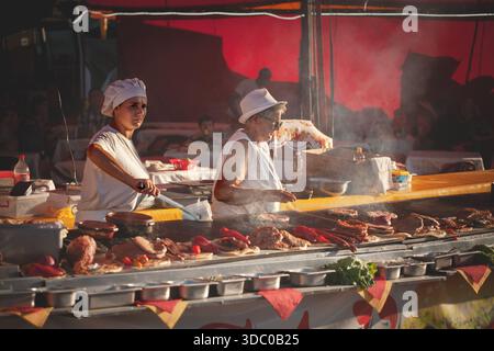 SABAC, SERBIA - SEPTEMBER 20, 2025: Two women working at a busy rostilj stand in Sabac, Serbia, grilling pljeskavica patties and other meats on a larg Stock Photo