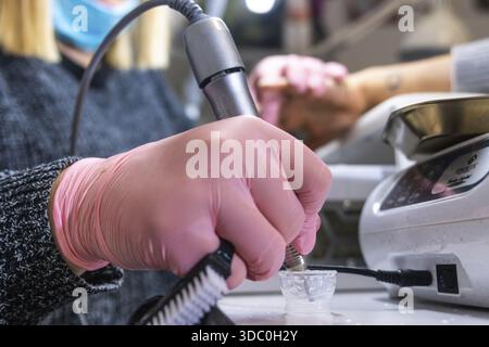Close-up of a nail technician preparing a nail drill for use, with focus on gloved hands Stock Photo