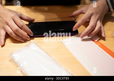 Close-up hands installing tempered glass screen protector on smartphone at table with cleaning kit. Concept of mobile protection, DIY repair, device m Stock Photo